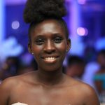Portrait of a smiling young woman with afro hair at an indoor event in Koforidua, Ghana.